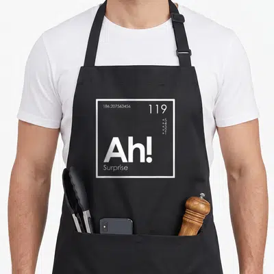 Surprise table apron - White square containing 119 Ah! Surprise and vertical plus signs — shown on a black cotton canvas apron against a white background