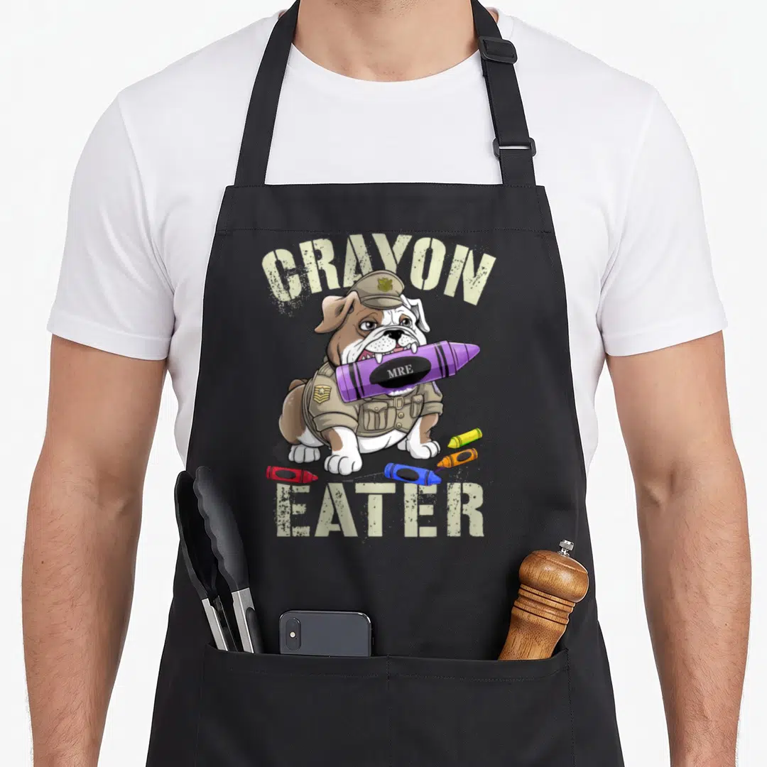 Crayon 4th of july apron - Bulldog in tan uniform holding purple MRE crayon with scattered red blue orange and yellow — shown on a black cotton canvas apron against a white background