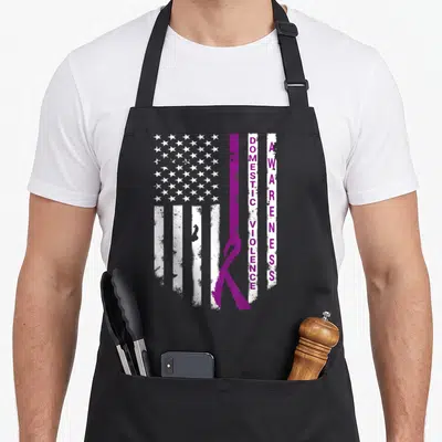 Prevention domestic aprons - Distressed US flag with purple ribbon and vertical DOMESTIC VIOLENCE AWARENESS text — shown on a black cotton canvas apron against a white background