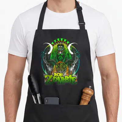 Rob eyed apron - Three-eyed monster head with horns, skulls, pentagram, and green Rob Zombie text — shown on a black cotton canvas apron against a white background
