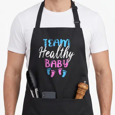 Shower healthy apron - Stacked TEAM Healthy BABY text in blue white pink with four alternating footprints — shown on a black cotton canvas apron against a white background