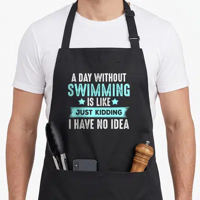Coach swimming apron - White and blue stacked text reading A DAY WITHOUT SWIMMING IS LIKE JUST KIDDING I HAVE NO IDEA — shown on a black cotton canvas apron against a white background