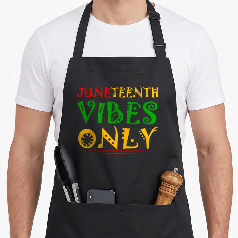 Melanin black apron - JUNETEENTH VIBES ONLY text in red yellow green with decorative line — shown on a black cotton canvas apron against a white background