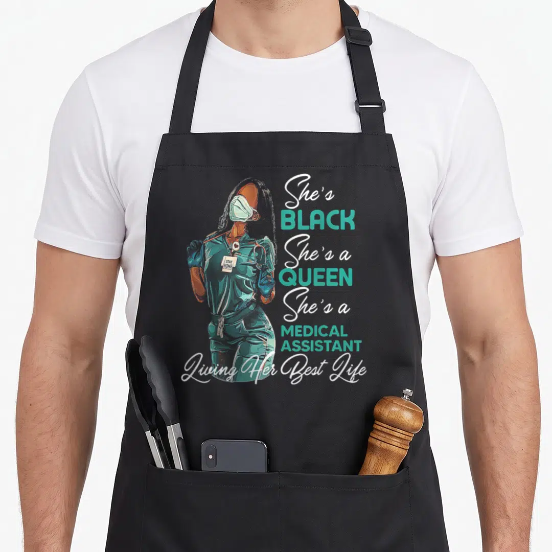 Medical queen apron - Realistic woman in teal scrubs and mask with She's Black She's a Queen text — shown on a black cotton canvas apron against a white background