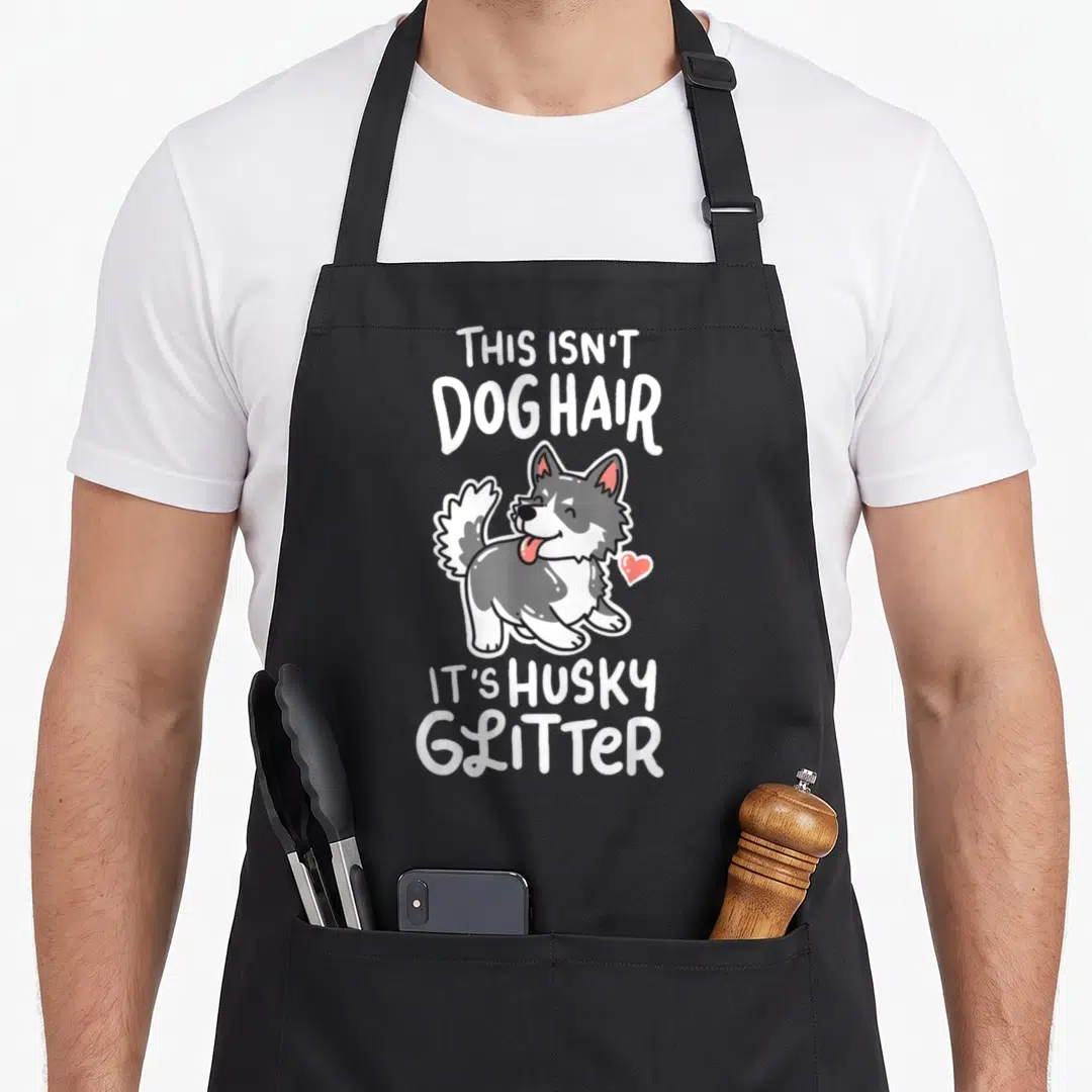 Owner husky apron - Cartoon grey and white husky centered between text reading This Isn't Dog Hair It's Husky Glitter — shown on a black cotton canvas apron against a white background