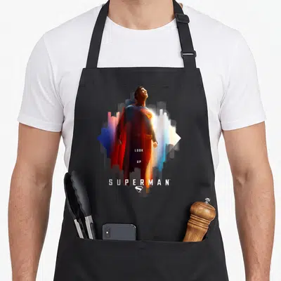 Shield novelty apron - Superman photo print with LOOK UP text and blue red white yellow colors — shown on a black cotton canvas apron against a white background