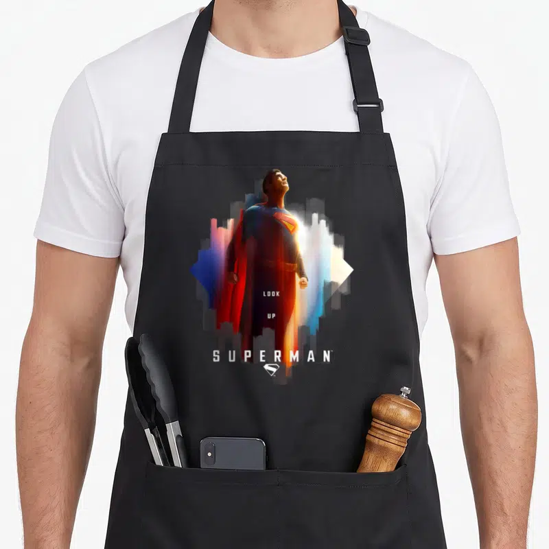 Shield novelty apron - Superman photo print with LOOK UP text and blue red white yellow colors — shown on a black cotton canvas apron against a white background