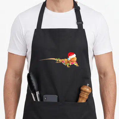 Bearded christmas apron - Bearded dragon wearing red Santa hat wrapped in orange red white blue yellow green Christmas — shown on a black cotton canvas apron against a white background