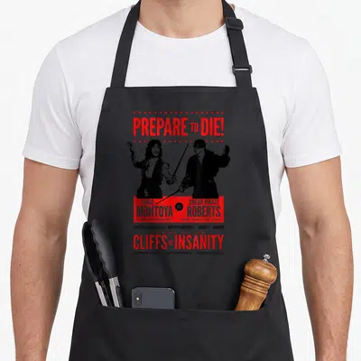 Inigo princess apron - Red and black duelist poster with Prepare to Die text and Cliffs of Insanity quote — shown on a black cotton canvas apron against a white background