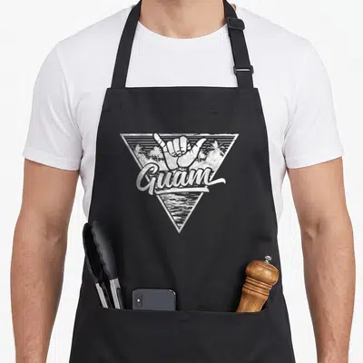 Shaka guam aprons - White distressed hand shaka sign inside triangle with palm trees and Guam text — shown on a black cotton canvas apron against a white background