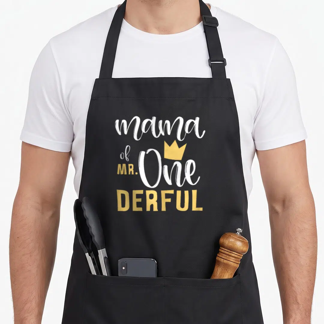 Onederful mama apron - White and yellow text reading mama of mr one derful with crown graphic — shown on a black cotton canvas apron against a white background