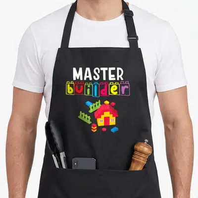 Builder building apron - Colorful toy house and brick letters spelling master builder on black fabric — shown on a black cotton canvas apron against a white background
