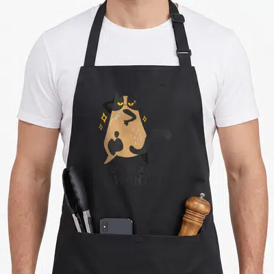 Personality cat apron - Cartoon tan and black cat posing with I DO WHAT I WANT text and yellow sparkles — shown on a black cotton canvas apron against a white background