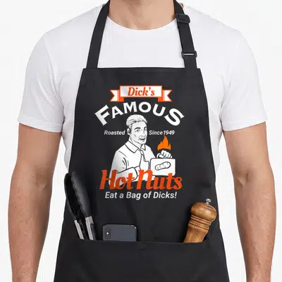 Hot famous aprons - Man holding flaming nut bag with Dick's FAMOUS Hot Nuts Eat a Bag of Dicks text in white and orange — shown on a black cotton canvas apron against a white background