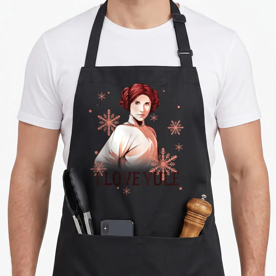 Leia christmas apron - Cartoon woman with I LOVE YULE text and pink snowflakes on white robe — shown on a black cotton canvas apron against a white background