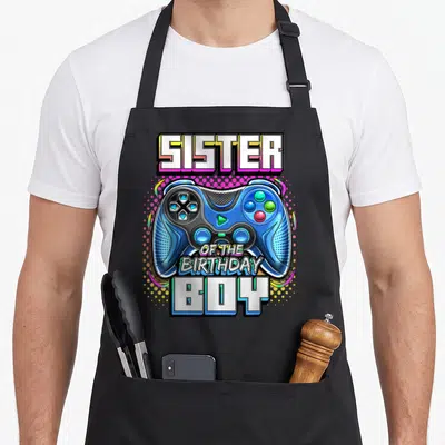 Sister birthday family video game apron - Blue game controller with SISTER OF THE BIRTHDAY BOY text and halftone — shown on a black cotton canvas apron against a white background