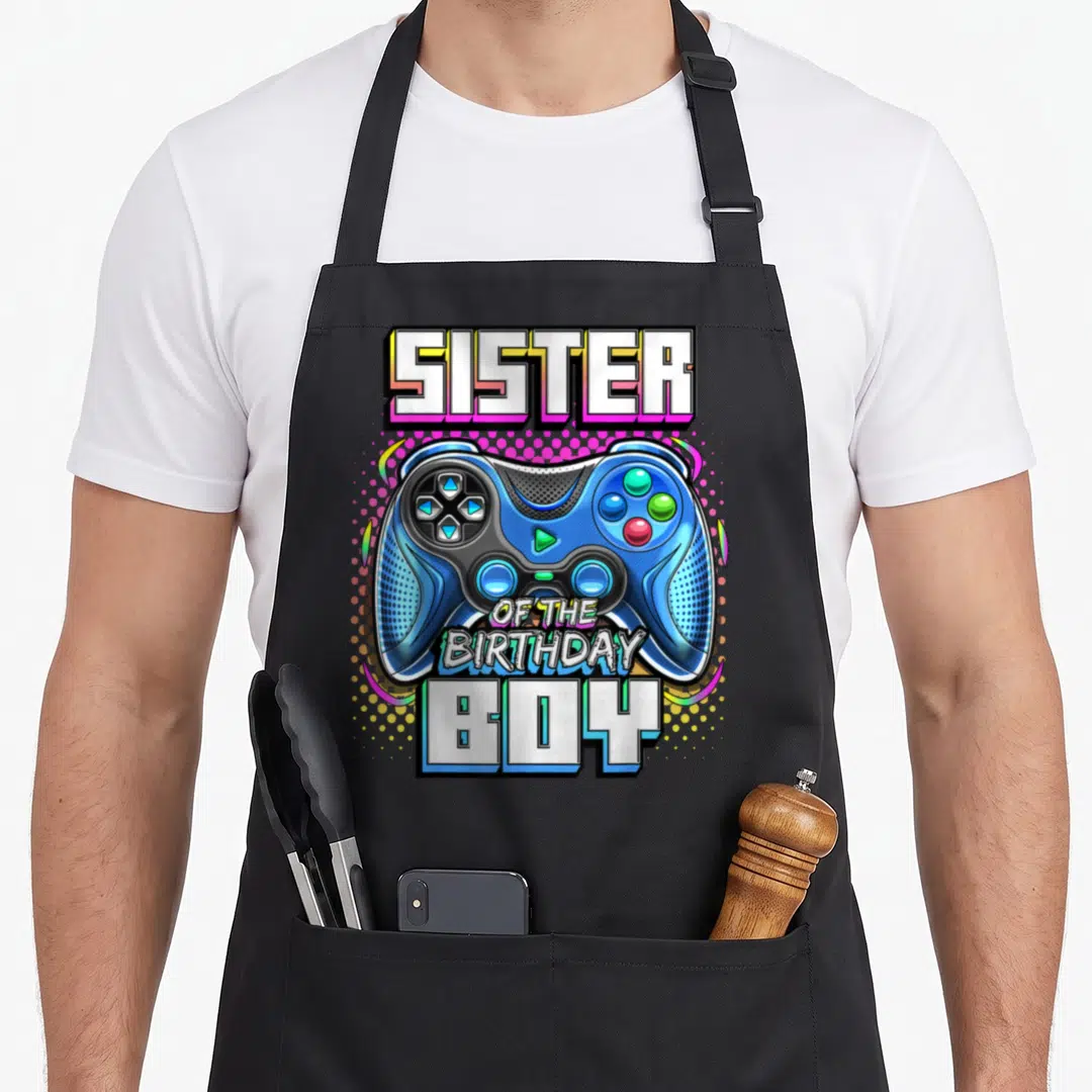Sister birthday family video game apron - Blue game controller with SISTER OF THE BIRTHDAY BOY text and halftone — shown on a black cotton canvas apron against a white background
