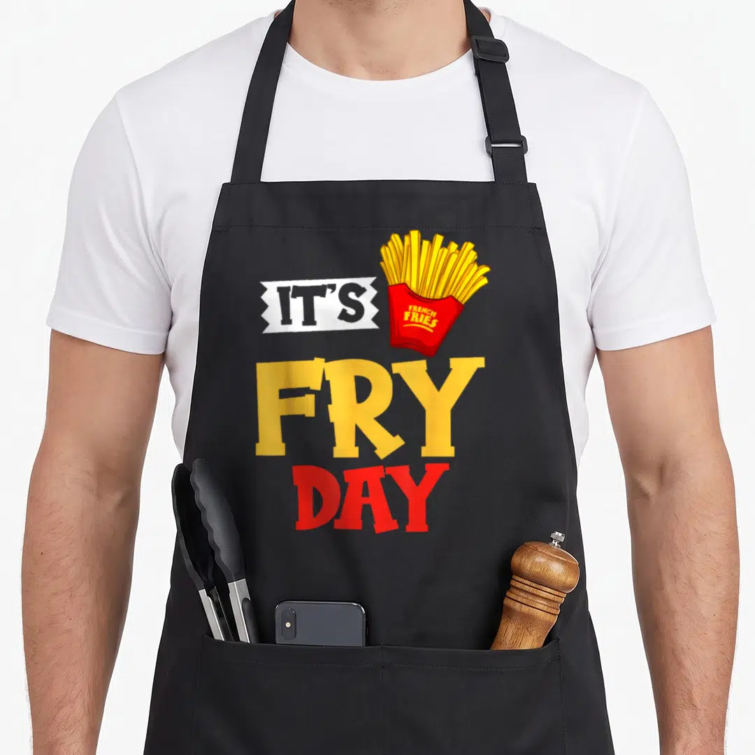 Fryer french apron - Cartoon yellow fries in red carton with It's Fry Day text — shown on a black cotton canvas apron against a white background