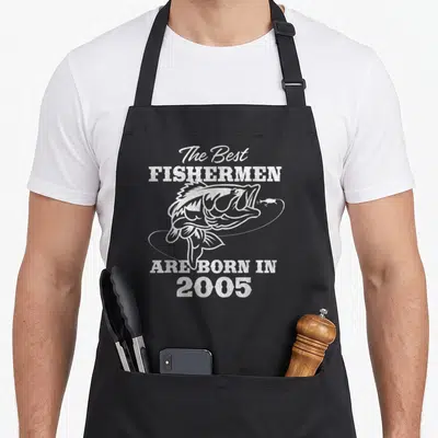 21st fishing aprons - White distressed fish with looping line and text The Best Fishermen Are Born In 2005 — shown on a black cotton canvas apron against a white background