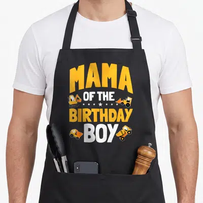 Mum construction worker apron - MAMA OF THE BIRTHDAY BOY text with four yellow construction vehicles and stars — shown on a black cotton canvas apron against a white background