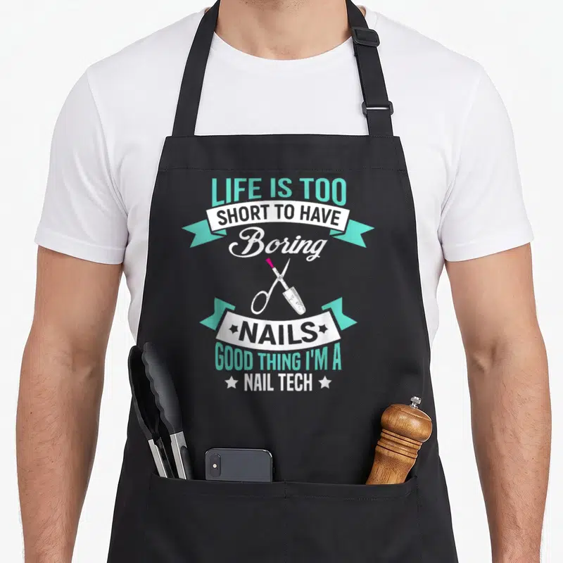Technician artist manicurist apron - Stacked teal text reading Life Is Too Short To Have Boring Nails with nail — shown on a black cotton canvas apron against a white background
