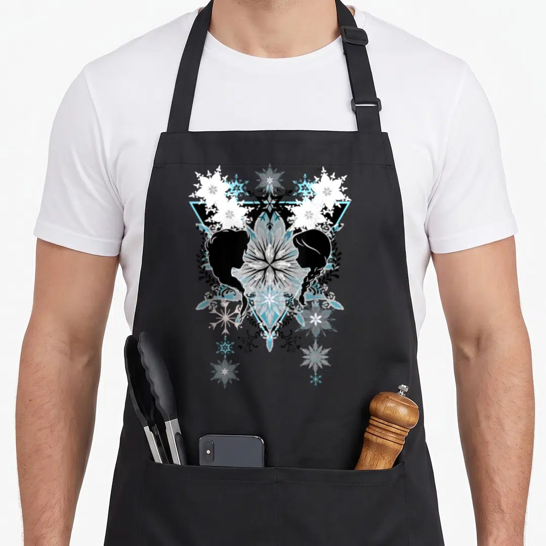 Anna boho apron - Two female silhouettes facing a snowflake mandala with leaves and a light blue triangle — shown on a black cotton canvas apron against a white background