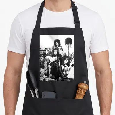 Queen promo aprons - Black and white photo of three men posing with a lamp and plants — shown on a black cotton canvas apron against a white background