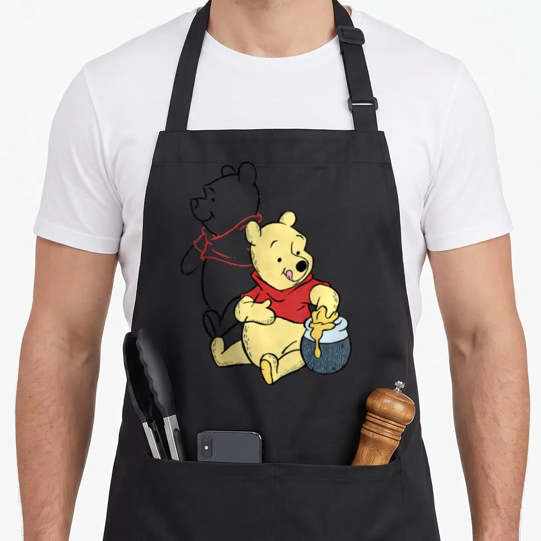 Portrait line apron - Cartoon Winnie the Pooh in yellow and red sitting with honey pot beside grey standing silhouette — shown on a black cotton canvas apron against a white background