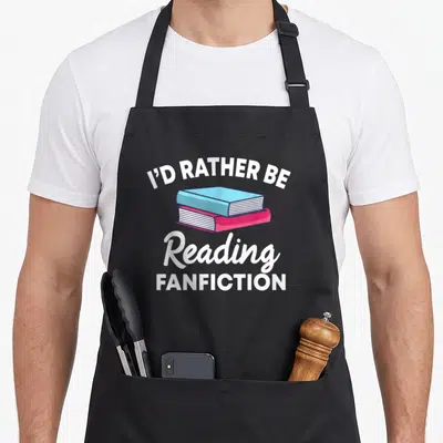 Would fan fiction apron - Two stacked books in blue and pink with I'D RATHER BE Reading FANFICTION text — shown on a black cotton canvas apron against a white background