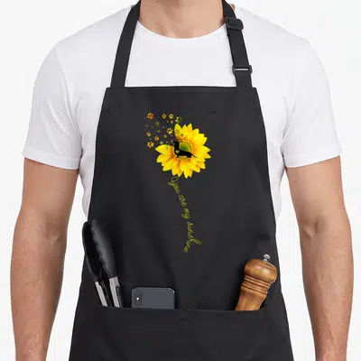 Sunshine dog apron - Yellow sunflower with black dog silhouette and You are my sunshine text — shown on a black cotton canvas apron against a white background