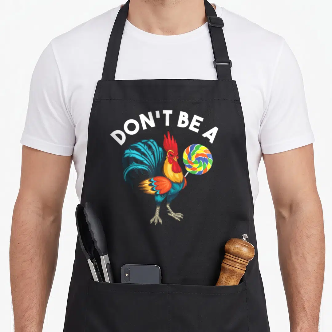 Sucker chicken apron - Cartoon rooster holding a multi-colored lollipop under white arched text — shown on a black cotton canvas apron against a white background