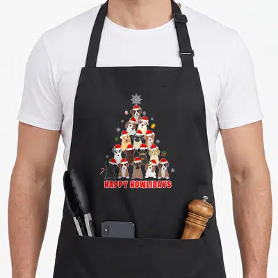 Funny dog christmas tree apron - Cartoon dogs in santa hats form a tree shape with happy howlidays text below — shown on a black cotton canvas apron against a white background