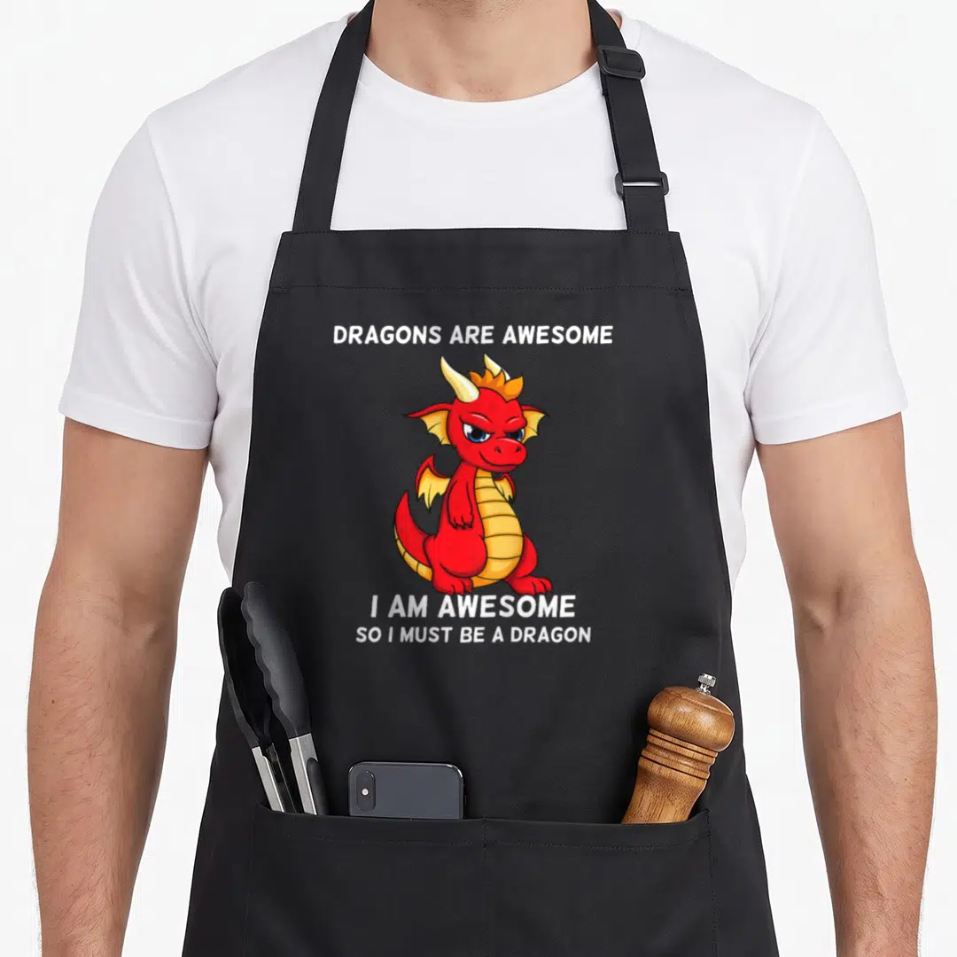 Cool dragon apron - Red cartoon dragon centered between white text reading Dragons Are Awesome I Am Awesome So I Must — shown on a black cotton canvas apron against a white background