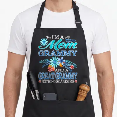 Scare grammy apron - Teal and blue text reading Mom Grammy Great Grammy with pink and blue flowers — shown on a black cotton canvas apron against a white background