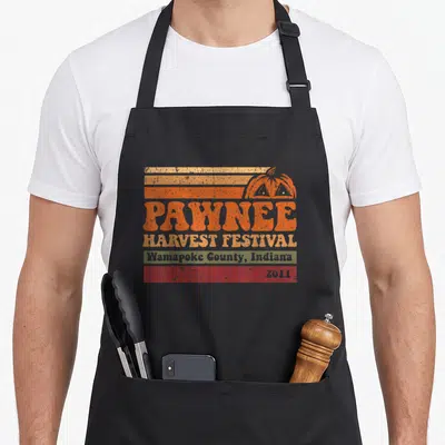 Funny music i love my hawk apron - Retro pumpkin and striped graphic with PAWNEE HARVEST FESTIVAL text and 2011 date — shown on a black cotton canvas apron against a white background