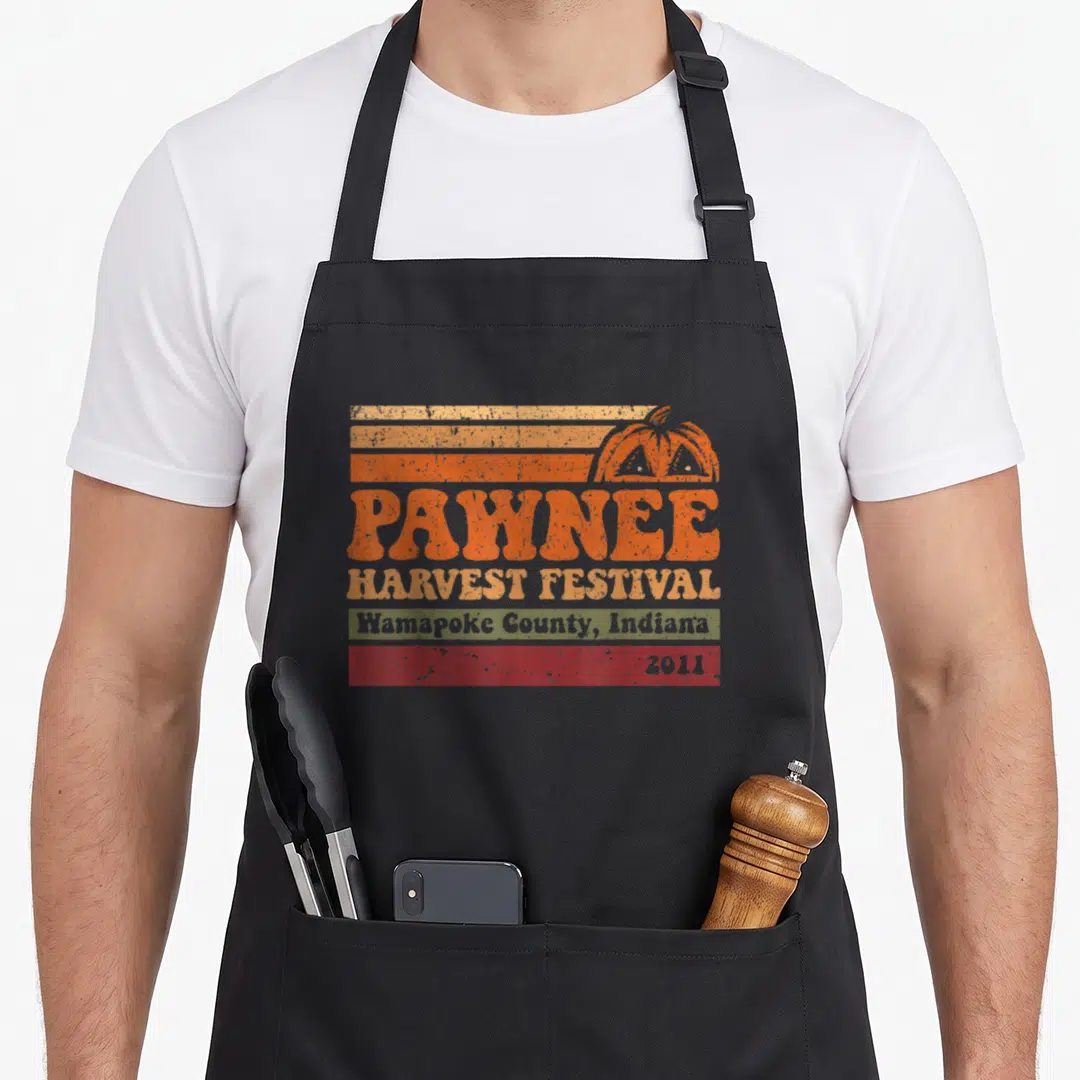 Funny music i love my hawk apron - Retro pumpkin and striped graphic with PAWNEE HARVEST FESTIVAL text and 2011 date — shown on a black cotton canvas apron against a white background
