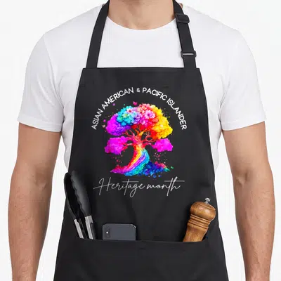 Colorful asian apron - Rainbow watercolor tree with flowers and ASIAN AMERICAN & PACIFIC ISLANDER Heritage month text — shown on a black cotton canvas apron against a white background
