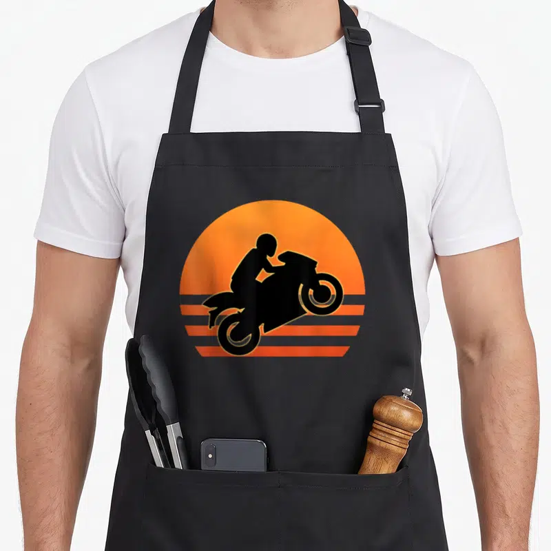 Wheelie motorcycle aprons - Black motorcyclist silhouette on orange sun with horizontal stripes — shown on a black cotton canvas apron against a white background