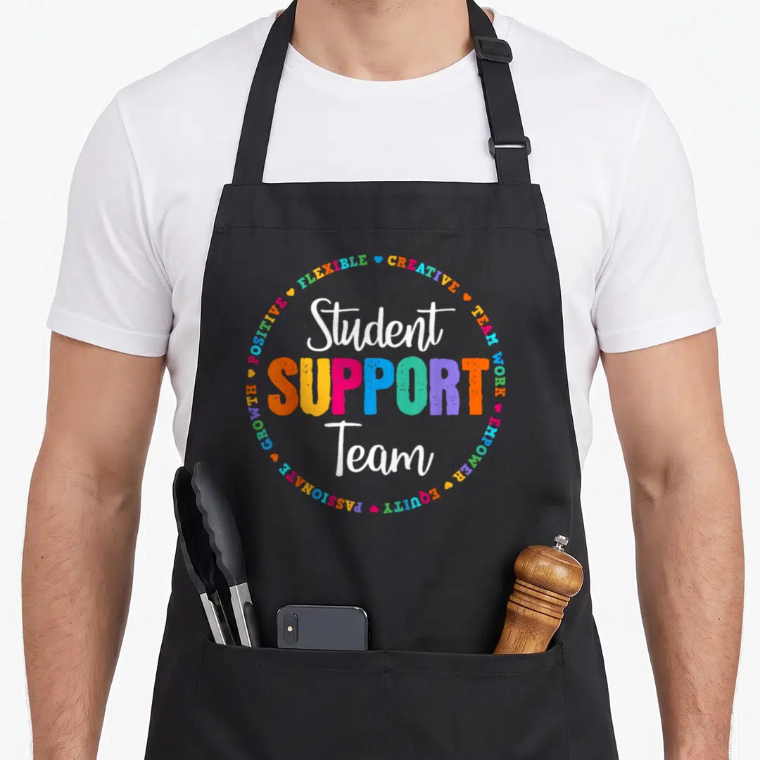 Student support teacher apron - Stacked Student SUPPORT Team text surrounded by colorful keywords and hearts in white — shown on a black cotton canvas apron against a white background