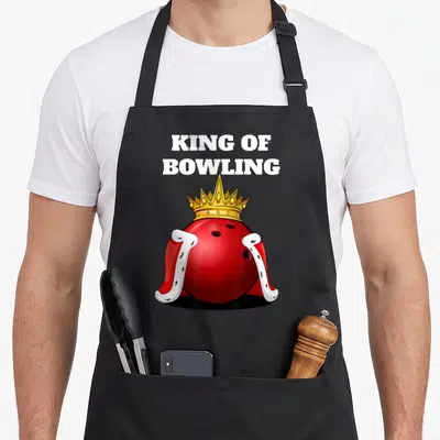 Bowling king apron - Red bowling ball wearing gold crown and red cape below white stacked text — shown on a black cotton canvas apron against a white background