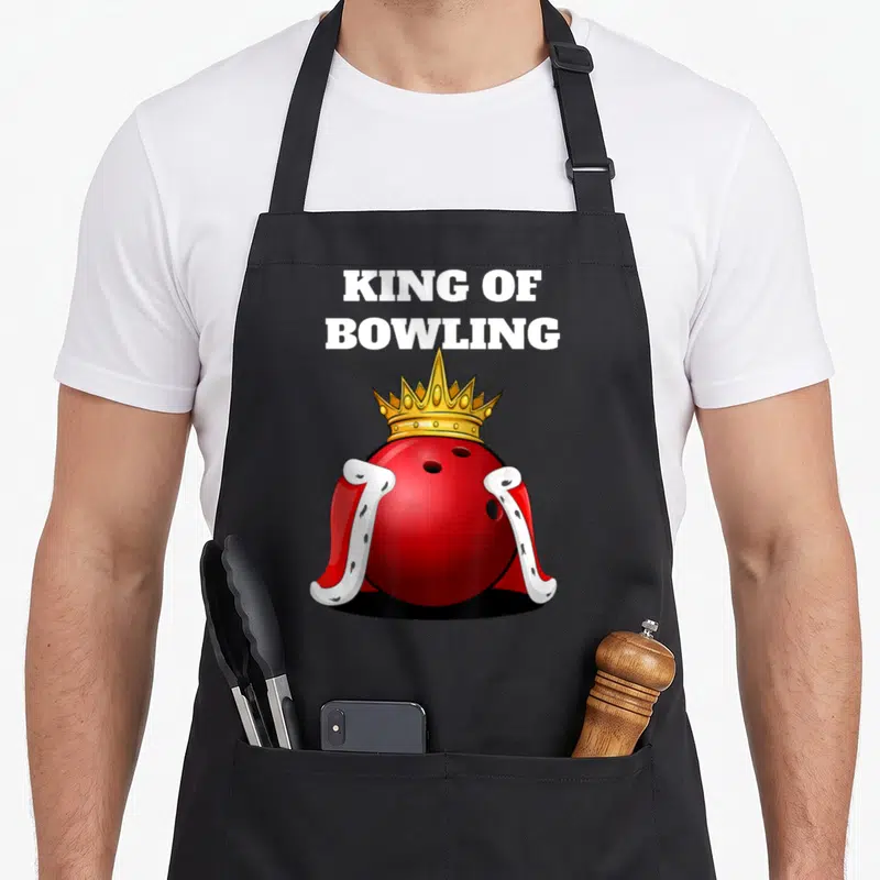 Bowling king apron - Red bowling ball wearing gold crown and red cape below white stacked text — shown on a black cotton canvas apron against a white background