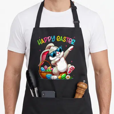 Dabbing bunny easter apron - Cartoon rabbit dabbing with sunglasses, basket of eggs, HAPPY EASTER text, colorful design — shown on a black cotton canvas apron against a white background