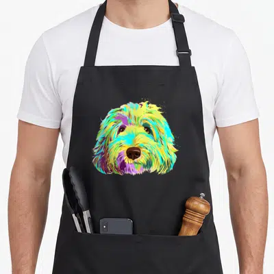 Colourful dog apron - Cartoon dog head in yellow cyan magenta and green colors with brown nose — shown on a black cotton canvas apron against a white background