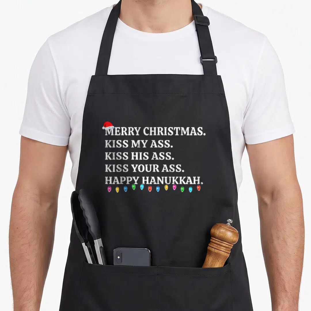 Christmas winter apron - Distressed white text reading Merry Christmas Kiss My Ass with Santa hat and multicolored — shown on a black cotton canvas apron against a white background