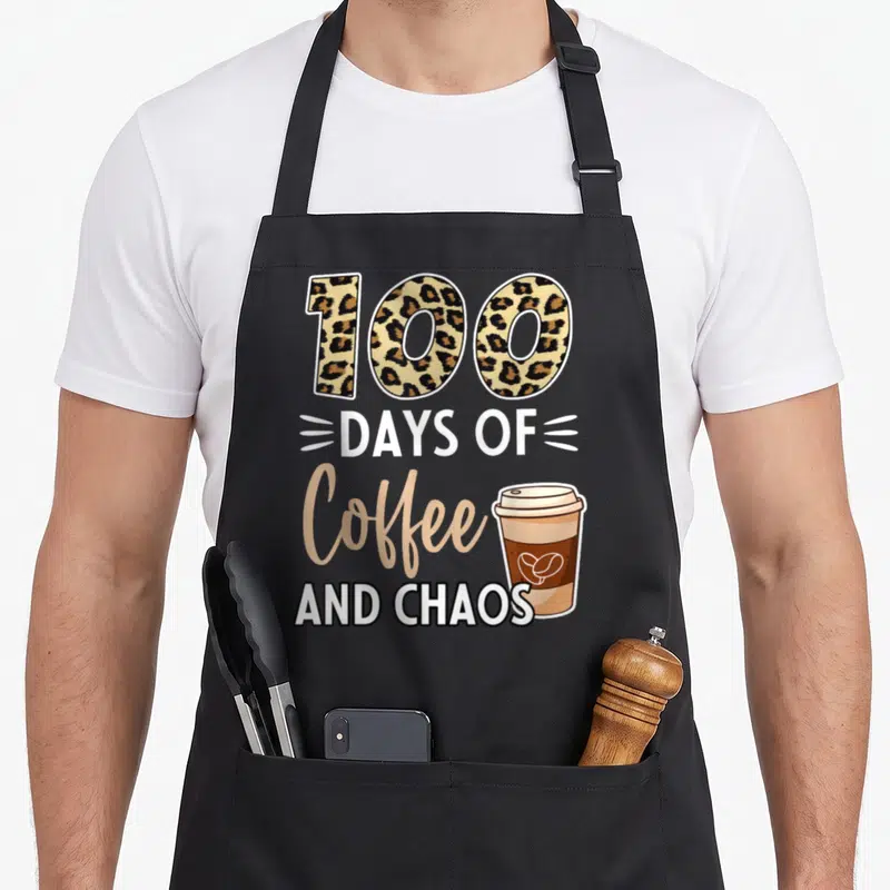 Coffee chao teacher apron - Leopard print 100, days of coffee and chaos text, and a brown takeaway coffee cup — shown on a black cotton canvas apron against a white background