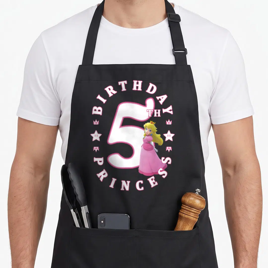 5th princess apron - Princess Peach standing next to large number 5 surrounded by BIRTHDAY PRINCESS text and crowns — shown on a black cotton canvas apron against a white background
