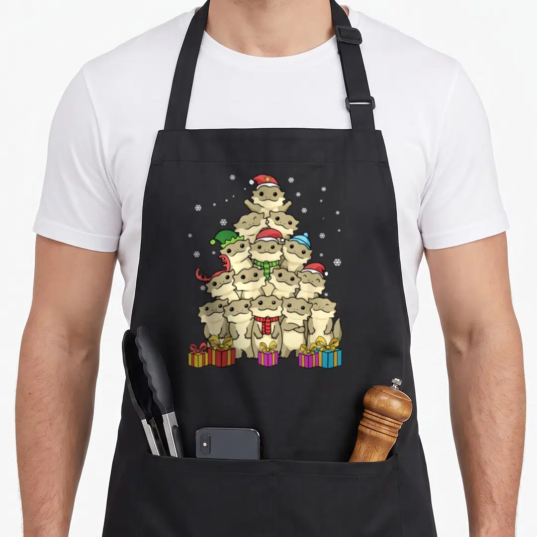 Bearded christmas tree apron - Cartoon reptiles stacked in a pyramid wearing festive hats and scarves with gift boxes — shown on a black cotton canvas apron against a white background