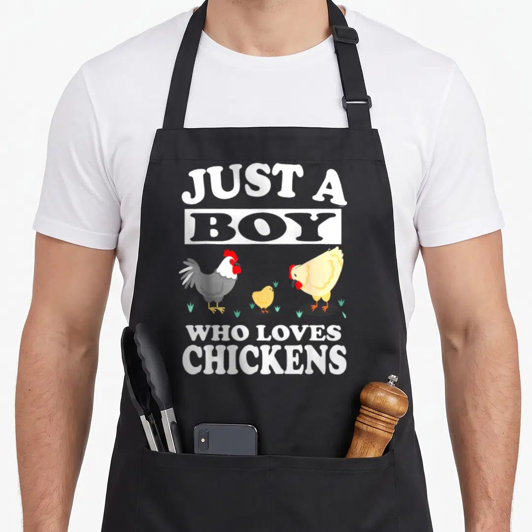 Farm chicken apron - Just A Boy Who Loves Chickens text with rooster hen and chick illustration — shown on a black cotton canvas apron against a white background