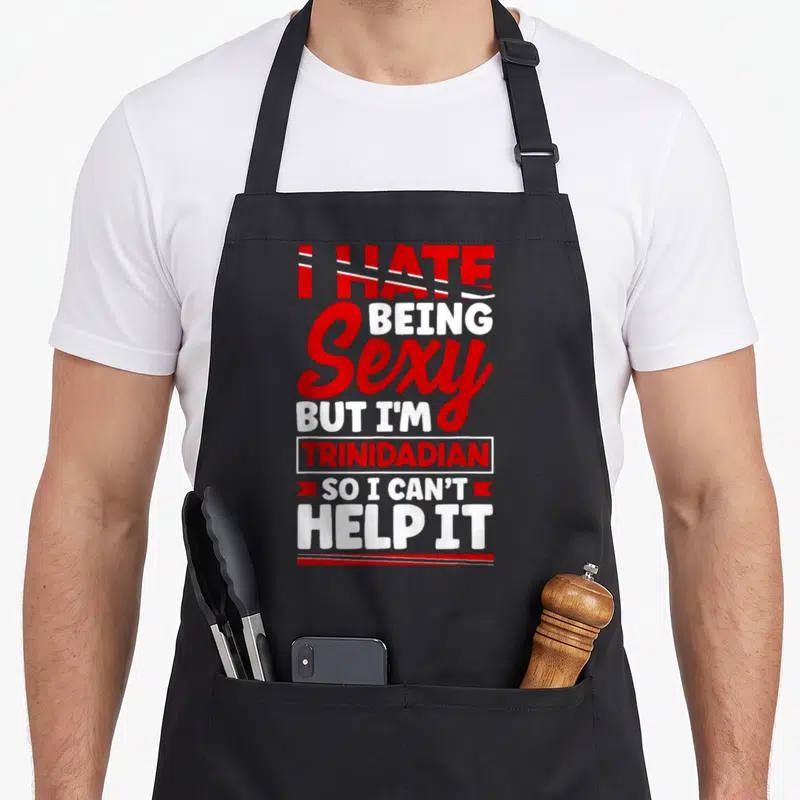 Trinidad lettering quotes apron - Stacked red and white text reading I HATE BEING Sexy BUT I'M TRINIDADIAN SO I CAN'T — shown on a black cotton canvas apron against a white background