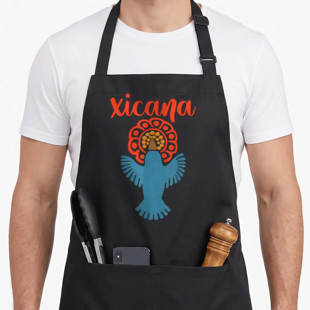 Chicana chicano mexican apron - Xicana script above blue bird with orange and yellow headdress — shown on a black cotton canvas apron against a white background